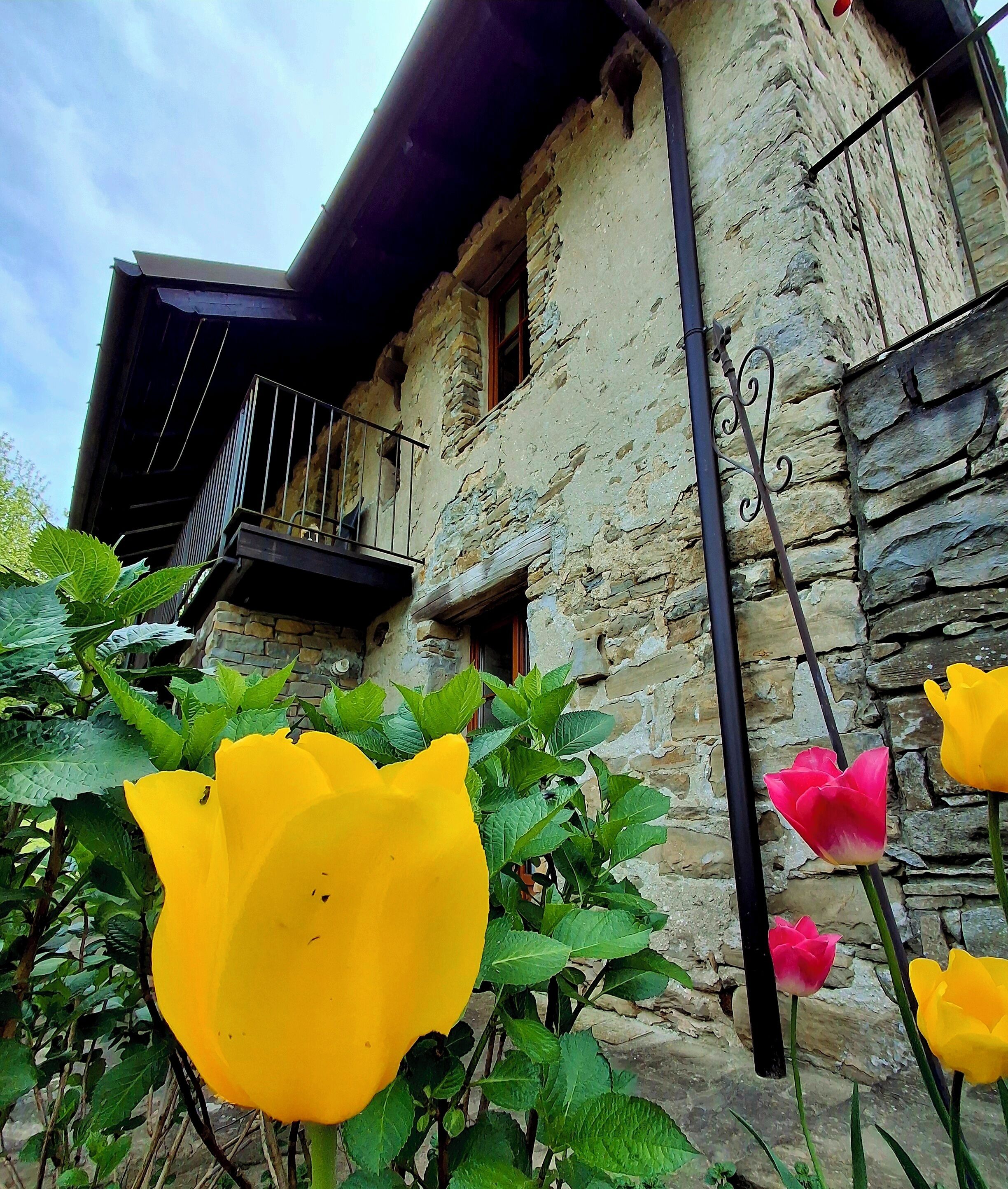 A rustic stone building with a balcony, a window, and a black metal railing.