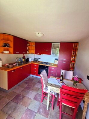 A compact kitchen with red cabinets, a dining table with chairs, and a window. - Charming Historic House in Provincia di Cuneo, Italia (Mombarcaro)