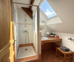 Une salle de bain avec une douche, un lavabo, un miroir et une petite fenĂȘtre.