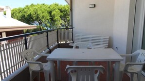 En balkon med et hvidt bord og stole, en hvid bænk og gelænder.