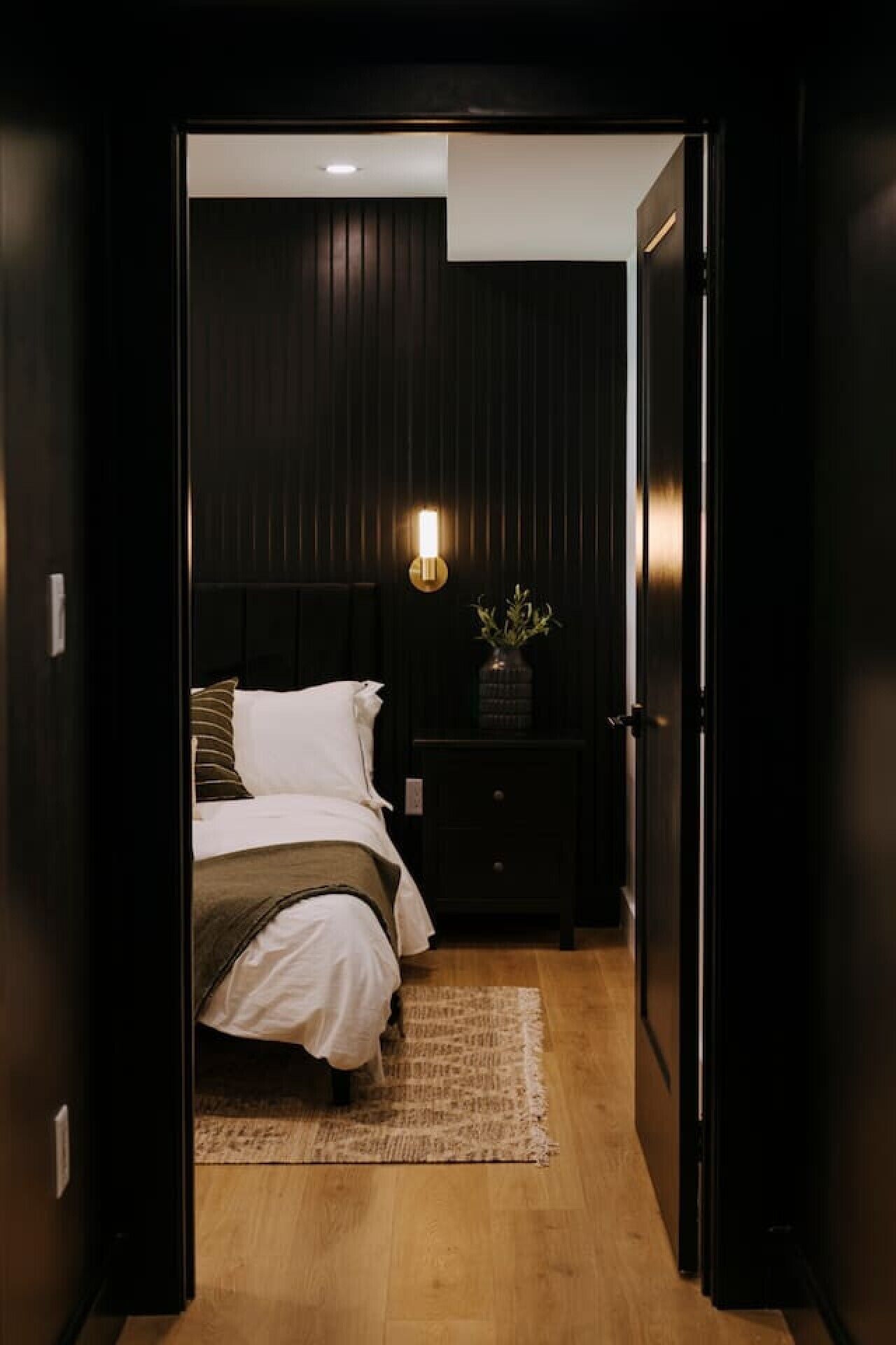A bedroom with a bed, bedside table, lamp, and a dark wooden wardrobe.
