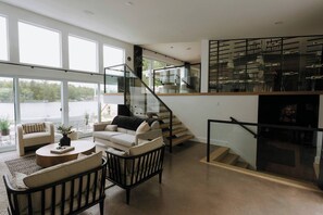 Un vaste espace de vie doté d’un escalier moderne, de grandes fenêtres et offrant une vue sur un plan d’eau.