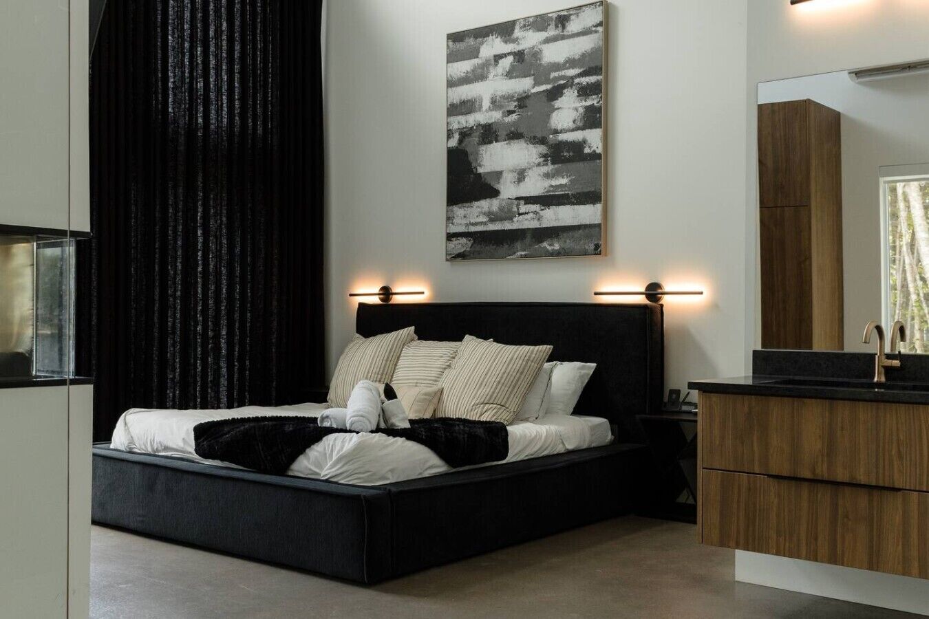 A modern bedroom with a black bed, white pillows, a black headboard, a wooden nightstand, and a large mirror.