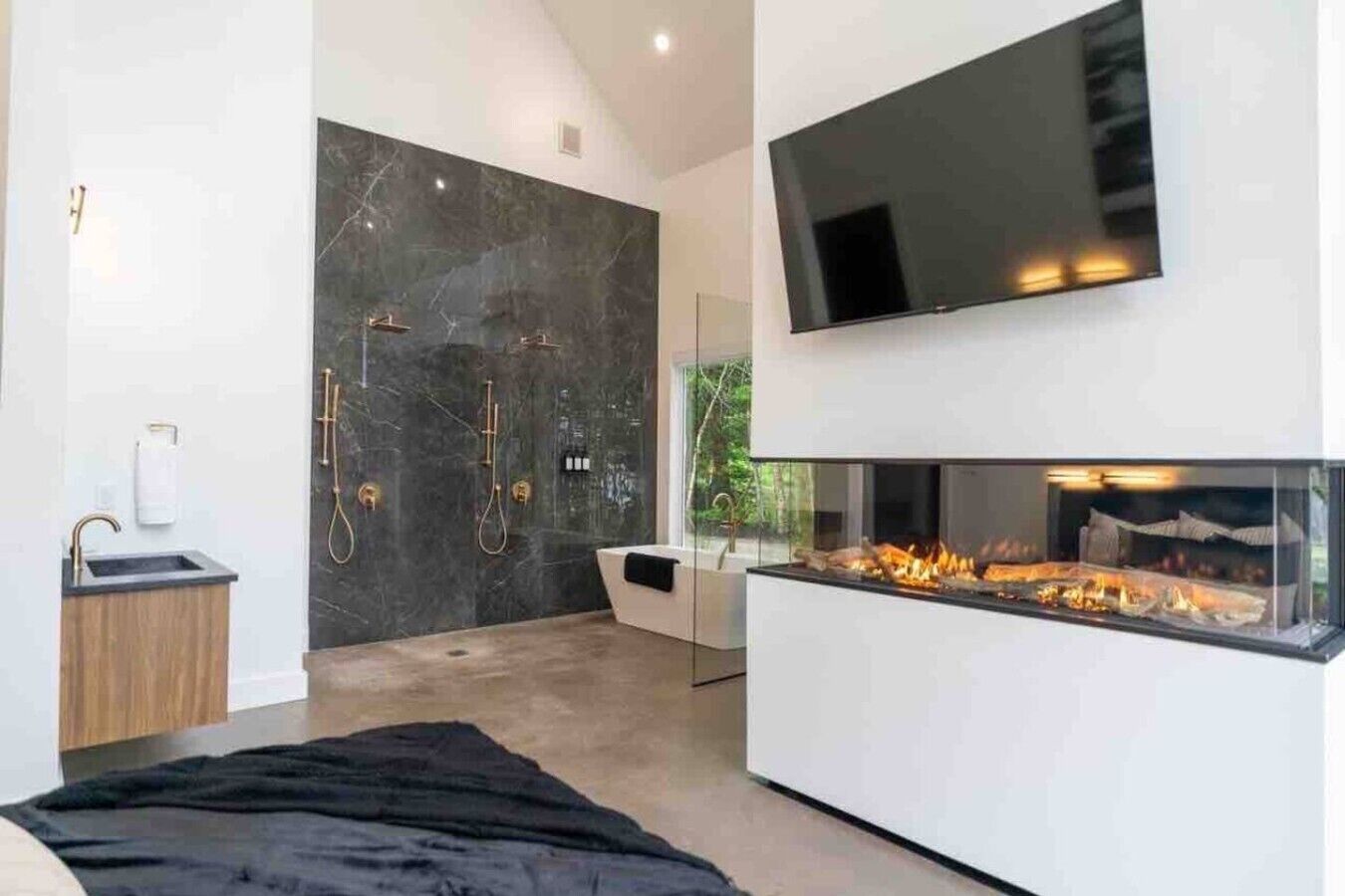 Een moderne badkamer met een marmeren wand, een badkuip en een tv aan de muur.