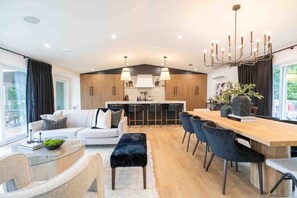 A modern kitchen with wooden cabinets, a dining area with a wooden table and chairs, and a living room with a sofa and a coffee table. - Elite Lakehouse w/ Hot Tub & Sauna (Mount Uniacke)