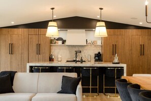 A modern kitchen with wooden cabinets, a marble countertop, and a central island with bar stools. - Elite Lakehouse w/ Hot Tub & Sauna (Mount Uniacke)