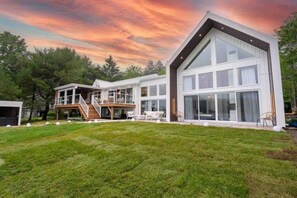 A modern two-story house with a large deck, a covered outdoor area, and a spacious lawn. - Elite Lakehouse w/ Hot Tub & Sauna (Mount Uniacke)
