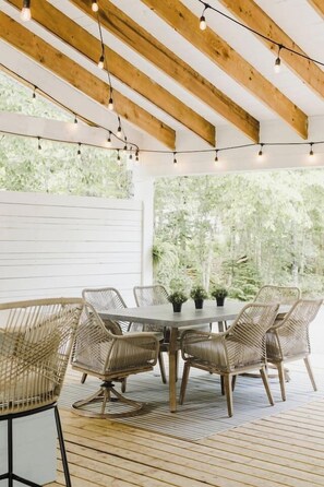 An outdoor patio with a wooden table and wicker chairs, surrounded by string lights.