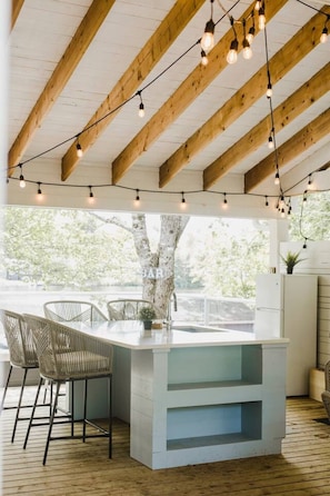A modern kitchen with a bar area, wooden ceiling beams, and string lights.