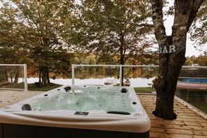 A hot tub on a wooden deck with a lake view, surrounded by trees.
