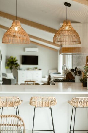 A modern kitchen with two hanging wicker pendant lights, a white countertop, and three wicker bar stools.