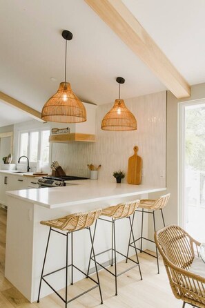A modern kitchen with a central island, two hanging wicker pendant lights, and a bar stool area.