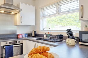 A modern kitchen with a stainless steel range hood, a built-in oven, a sink with a dish rack, and a window with blinds. - 2 Bed Bungalow| Parking| Garden Leigh-on-Sea (Southend-on-Sea)