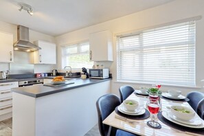 A modern kitchen with a central island, white cabinetry, and a dining area with a table set for two. - 2 Bed Bungalow| Parking| Garden Leigh-on-Sea (Southend-on-Sea)