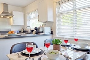 A modern kitchen with white cabinets, a microwave, and a sink. There is a dining table set with plates, glasses, and a bowl of salad. - 2 Bed Bungalow| Parking| Garden Leigh-on-Sea (Southend-on-Sea)