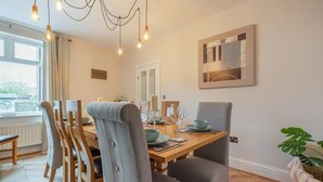 A dining area with a wooden table, grey upholstered chairs, and pendant lighting. - 4 Bed in Whitby (oc-w42084) (Whitby)