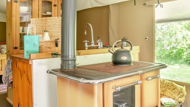 A compact kitchen with a stove, kettle, and wooden cabinets.