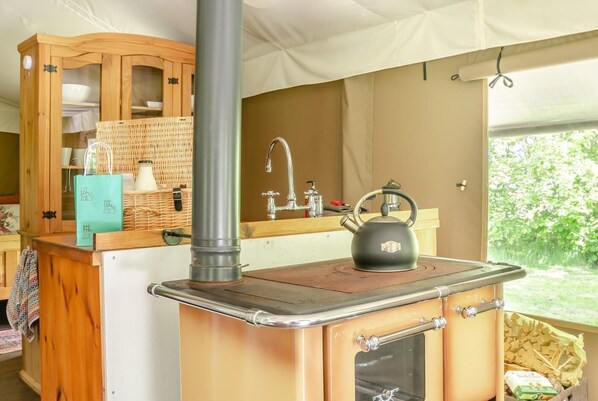 A compact kitchen with a stove, kettle, and wooden cabinets.