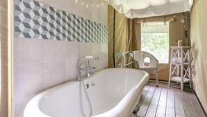 A bathroom with a freestanding bathtub, a shower, and a window with curtains.