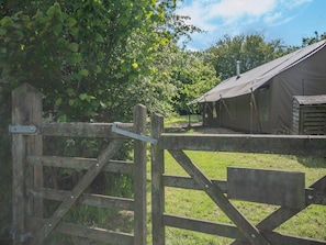 A rustic wooden gate leading to a campsite with a tented accommodation structure.