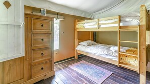 A bunk bed room with a wooden dresser, a small window, and a patterned rug.