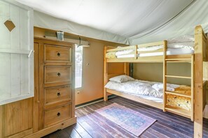 A bunk bed room with a wooden dresser, a small window, and a patterned rug.