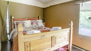 A wooden bed with floral bedding, a canopy, and a view of greenery outside.