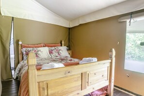 A wooden bed with floral bedding, a canopy, and a view of greenery outside.