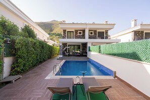 A modern pool area with a view of a two-story building, a wooden deck, and a green lawn.