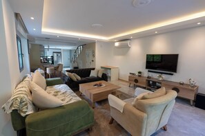 A modern living room with a sofa, armchairs, a coffee table, a TV, and a staircase leading to a kitchen.