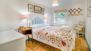 Ein Schlafzimmer mit Bett, Nachttischlampen, einem Fenster, einem Sessel und Wandbildern.
