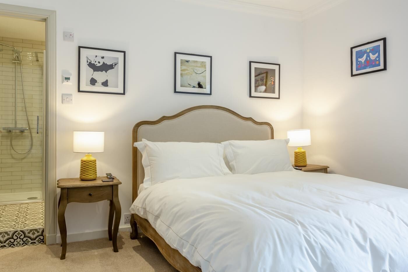 A hotel room with a bed, two bedside tables with lamps, a shower, and three framed pictures on the wall.