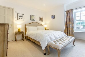 A bedroom with a bed, bedside tables, a bench, and a window with curtains.