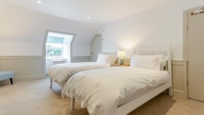 Une chambre avec deux lits, un banc, une fenêtre et une porte.