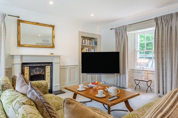 A living room with a fireplace, a television, a bookshelf, and a window with curtains.