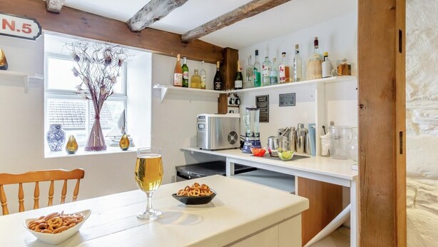 Une cuisine avec une table à manger, un verre de bière, un bol de bretzels, un mixeur et diverses bouteilles rangées sur des étagères.