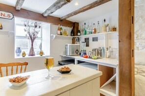 Una cocina con una mesa de comedor, una jarra de cerveza, un cuenco de pretzels, una licuadora y una variedad de botellas en estanterías.