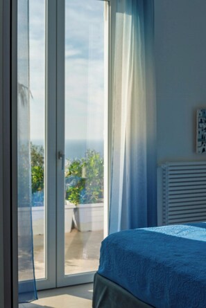 Ein Schlafzimmer mit Bett, einem Fenster mit Vorhängen und Blick ins Grüne.