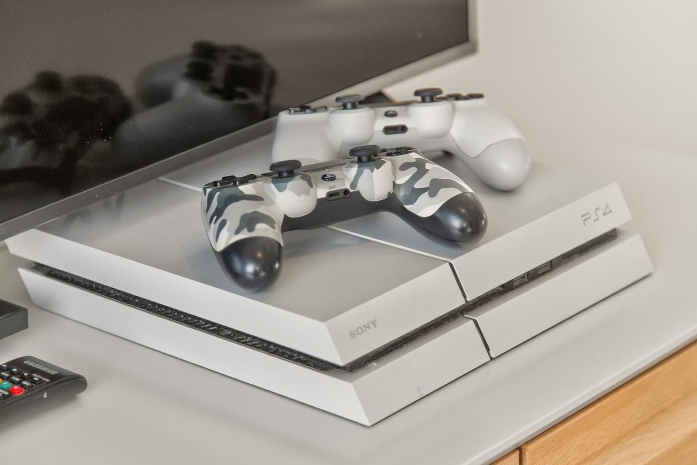 Eine PlayStation 4 Konsole mit zwei Controllern auf einem weißen Regal.