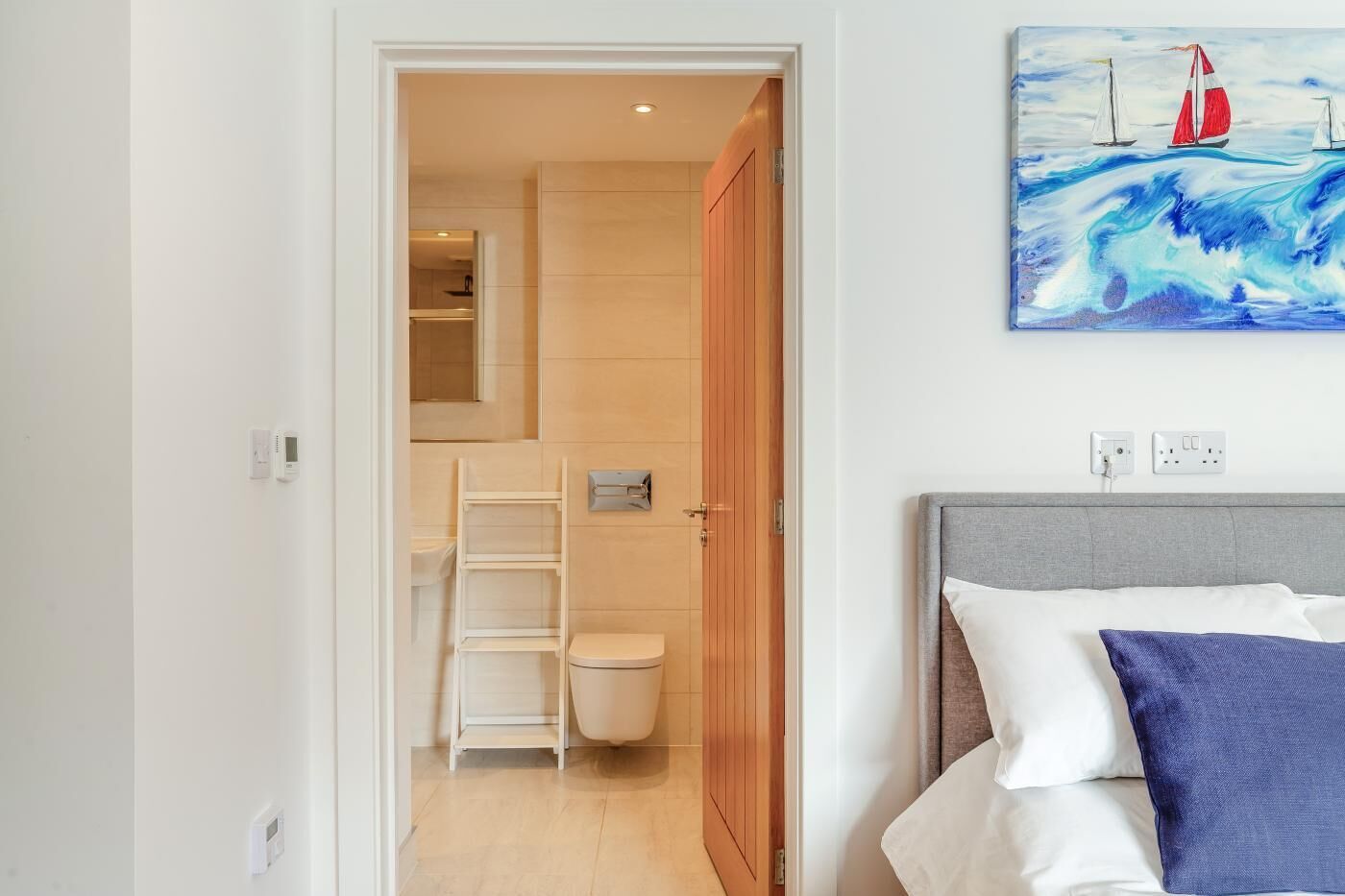 A hotel room with a bed, a painting of sailboats, a wooden door, and a white toilet.