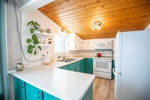 A kitchen with white cabinets, a teal countertop, a wooden ceiling, and a white refrigerator. - The Lily Pad - Charming Lakefront w/ Hot tub (Mount Uniacke)