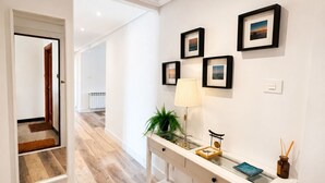 En gang med et hvidt konsolbord, billeder i rammer, en lampe og et skilt med ordet 'home' på væggen.