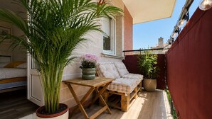 En balkon med et træbord, en siddeplads med hynder og krukker med planter.