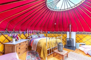 A yurt with a bed, wooden dresser, and a wood-burning stove.