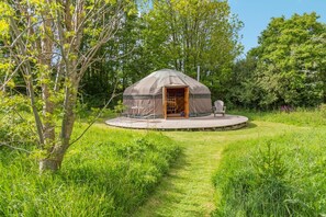 A yurt with an open door, a deck, and a chair outside.