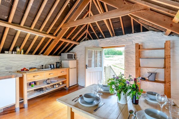 An attic-style kitchen with wooden beams, a dining table set for four, and a view of the outdoors.