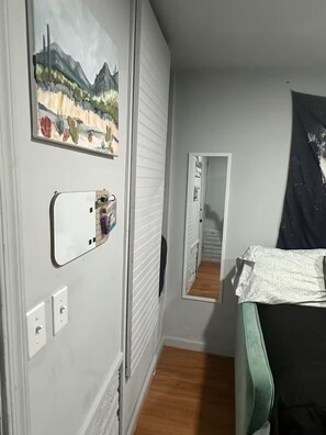 Ein Schlafzimmer mit Bett, einem Gemälde, einem Spiegel und einer Tür.