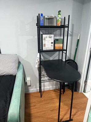 Ein Zimmer mit einem Bett, einem schwarzen Metallregal mit Gegenständen, einem grünen Stuhl und einem Besen.
