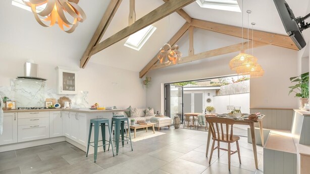 A spacious kitchen with a central island, wooden beams, and a dining area with a table and chairs. - 3 Bed in Falmouth (oc-o42451) (Falmouth)