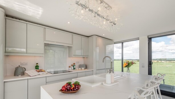Een moderne keuken met witte kastjes, een centraal eiland met een fruitschaal, en uitzicht op de omgeving.